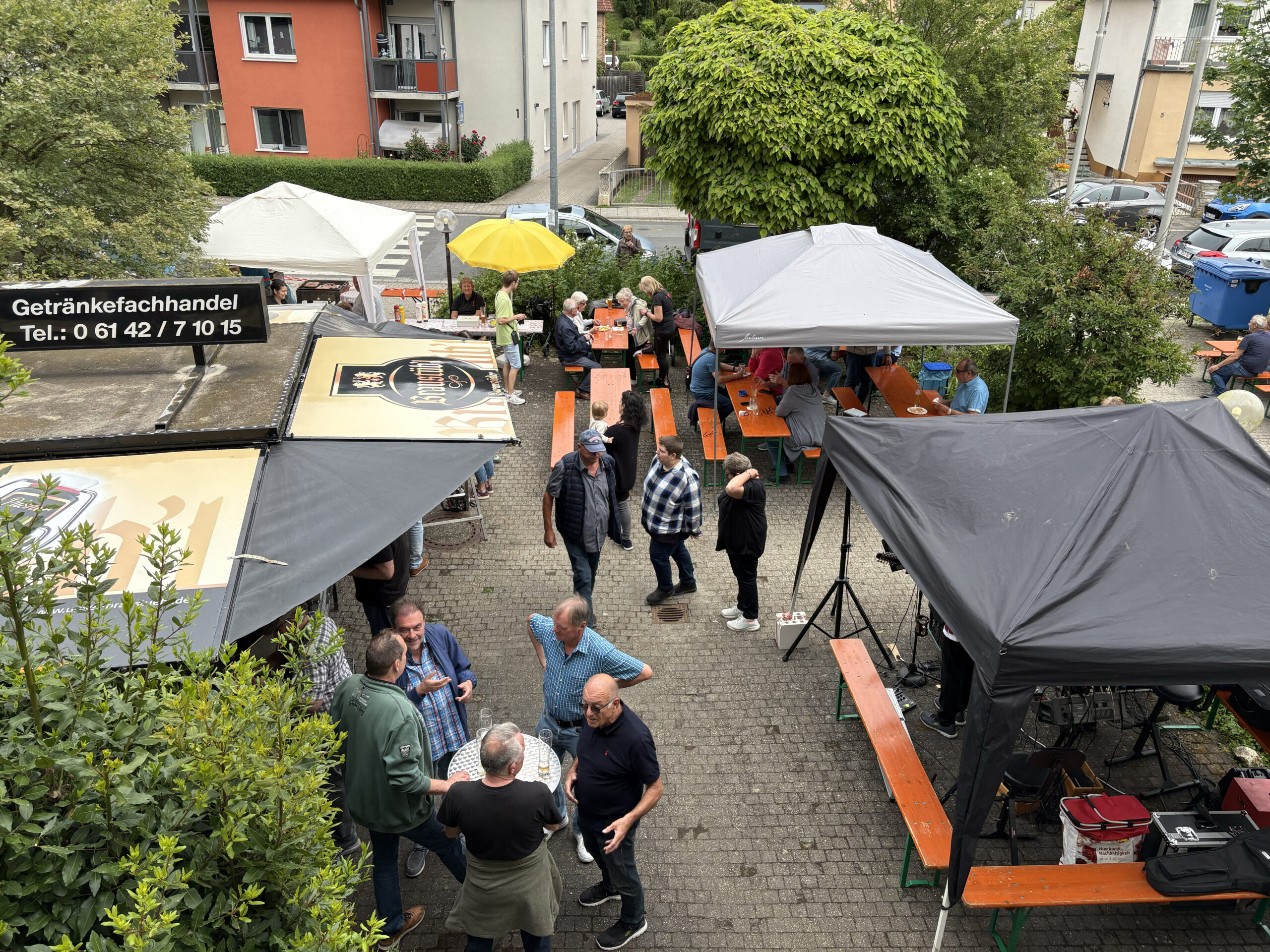 Blick von oben auf den Außenbereich des Sängerfrühschoppens am Vatertag 2025 mit Verkaufsständen für Getränke und Gegrilltes sowie geselligem Beisammensein unter Pavillons.
