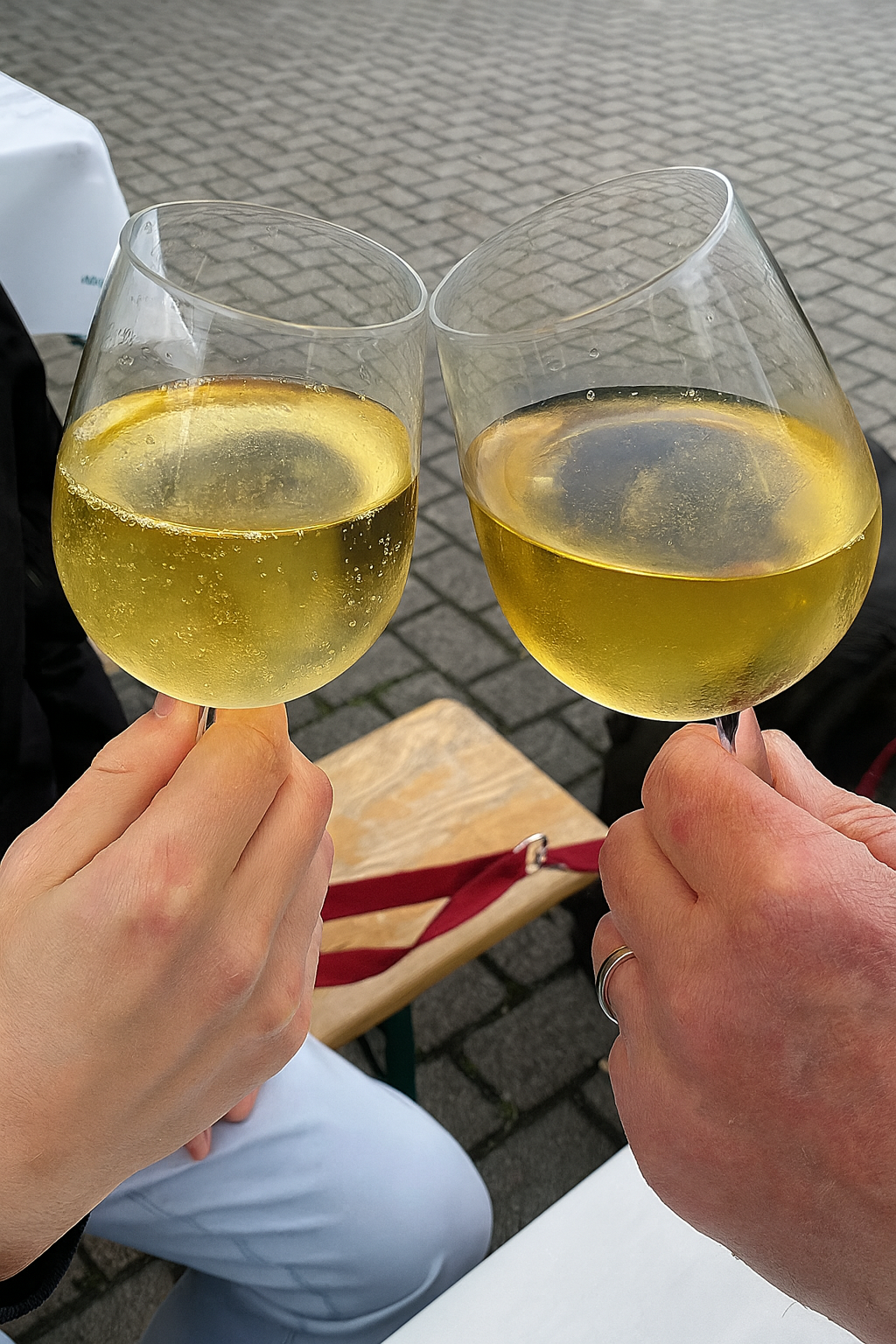 Zwei Personen stoßen mit Gläsern Weißwein beim Weinstand des Frauenchors Lorsbach an.