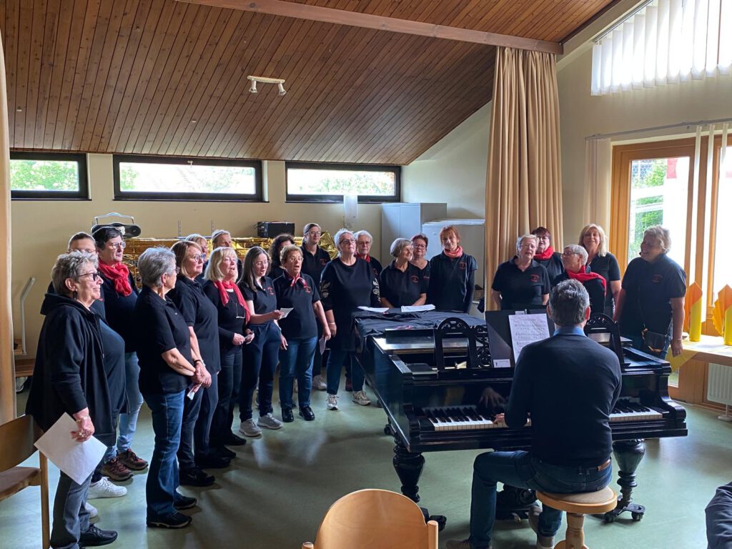 Auftritt des Frauenchors Lorsbach beim Sängerfrühschoppen am Vatertag im evangelischen Gemeindehaus in Lorsbach. Die Sängerinnen stehen halbkreisförmig um einen Flügel und singen gemeinsam unter der Leitung von Dirigent Konstantin Karklisiyski.