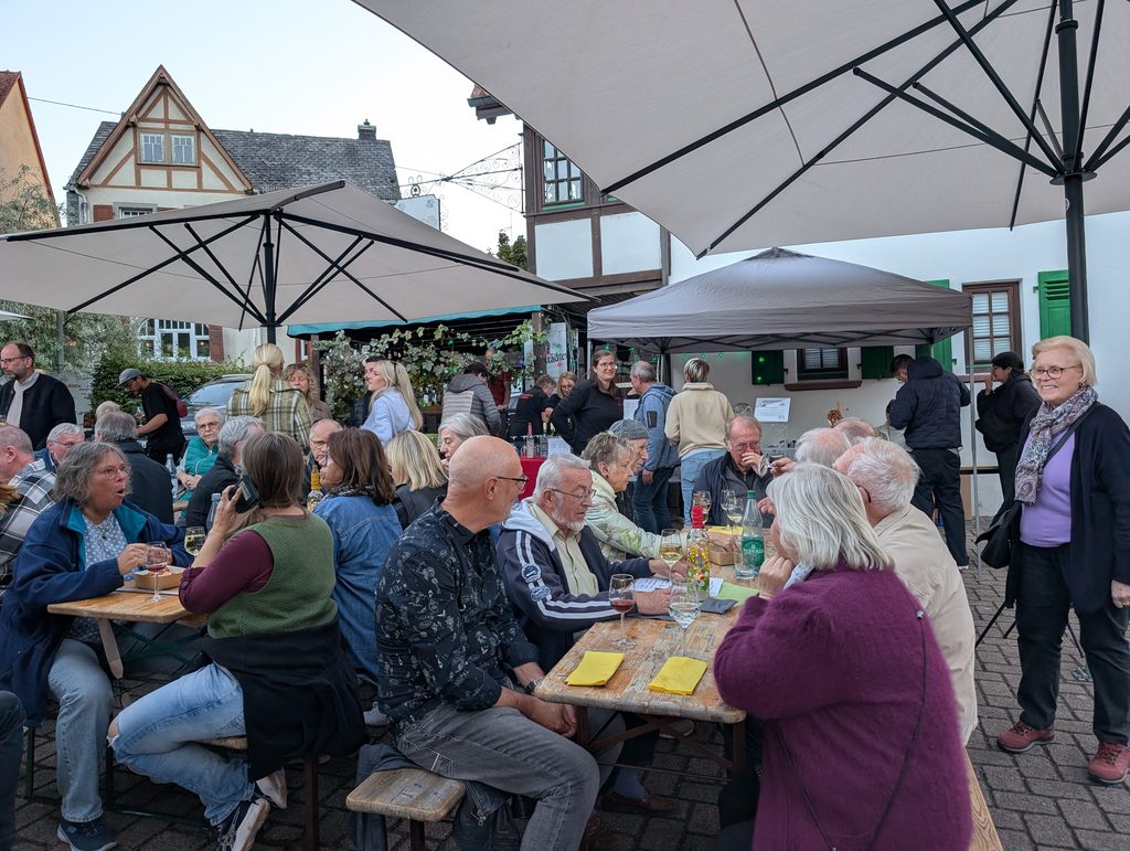 Gäste sitzen beim Weinstand 2026 an Biertischen unter Sonnenschirmen